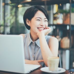 Smiling woman holding her chin with a laptop and a cup next to her