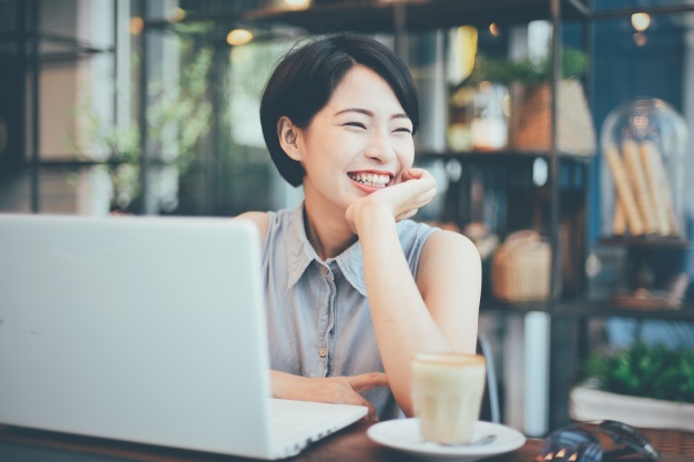 Smiling woman holding her chin with a laptop and a cup next to her