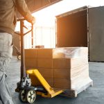 : a man is delivering a stack of boxes wrapped in plastic for secure shipping