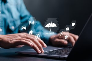 Business professional's hands typing on laptop with digital insurance icons including umbrella, car, home, and family.